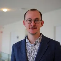 Kjetil Erdogan Lavik, wearing glasses and a blue jacket, in a bright office corridor.